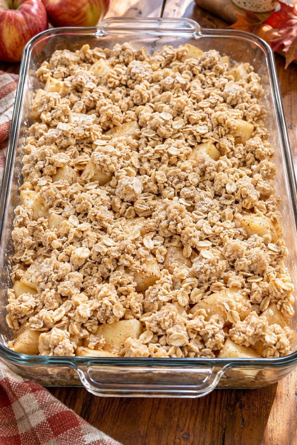 Unbaked rolled oat crumbs scattered over cinnamon apples in glass baking dish